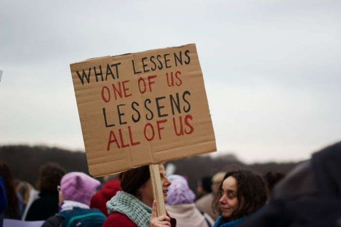 protester holding sign saying 'what lessens one of us lessens all of us'